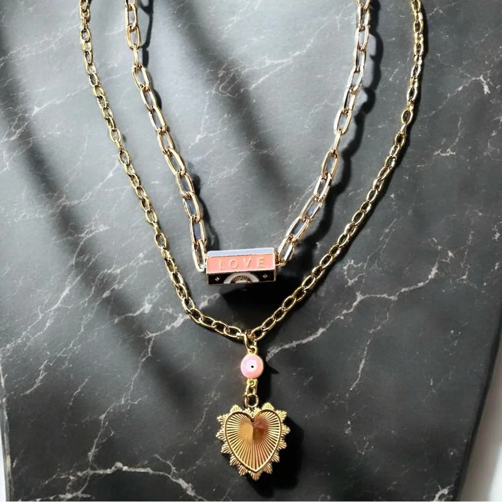 Gold toned chains with black, white, gold, and pastel pink enamel charms.